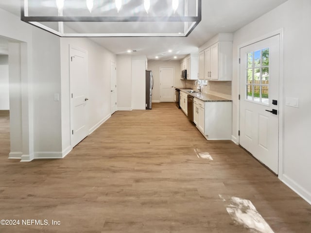 kitchen with a sink, white cabinetry, baseboards, appliances with stainless steel finishes, and light wood finished floors