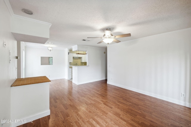 unfurnished living room featuring ornamental molding, ceiling fan, a textured ceiling, wood finished floors, and baseboards