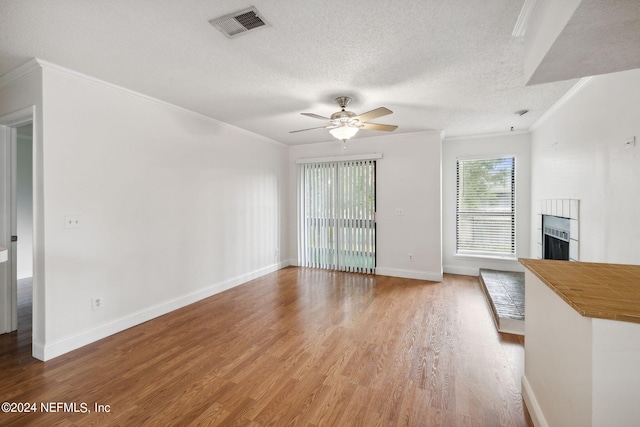 unfurnished living room featuring visible vents, a tile fireplace, wood finished floors, crown molding, and a textured ceiling