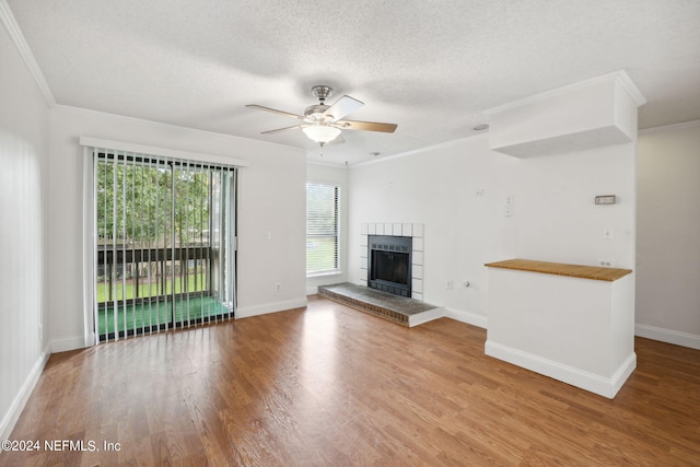 unfurnished living room with a textured ceiling, ornamental molding, a tiled fireplace, and wood finished floors