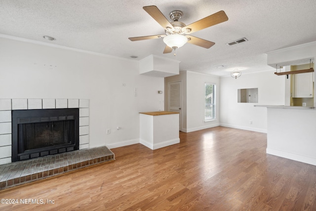 unfurnished living room with ornamental molding, a brick fireplace, visible vents, and wood finished floors