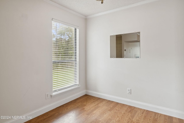 empty room with a textured ceiling, ornamental molding, light wood-style flooring, and baseboards