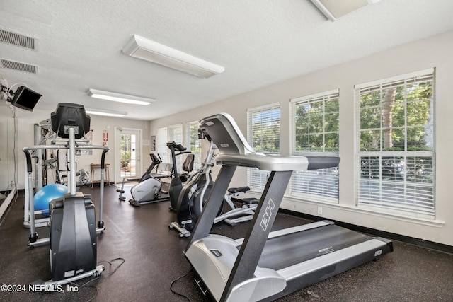 exercise room with visible vents, a textured ceiling, and baseboards