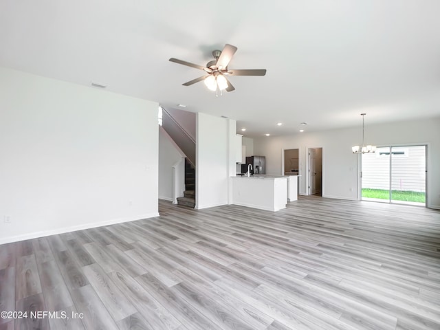 unfurnished living room featuring light wood-type flooring, ceiling fan with notable chandelier, and sink