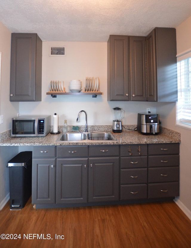 kitchen featuring dark hardwood / wood-style floors, sink, a textured ceiling, and light stone counters