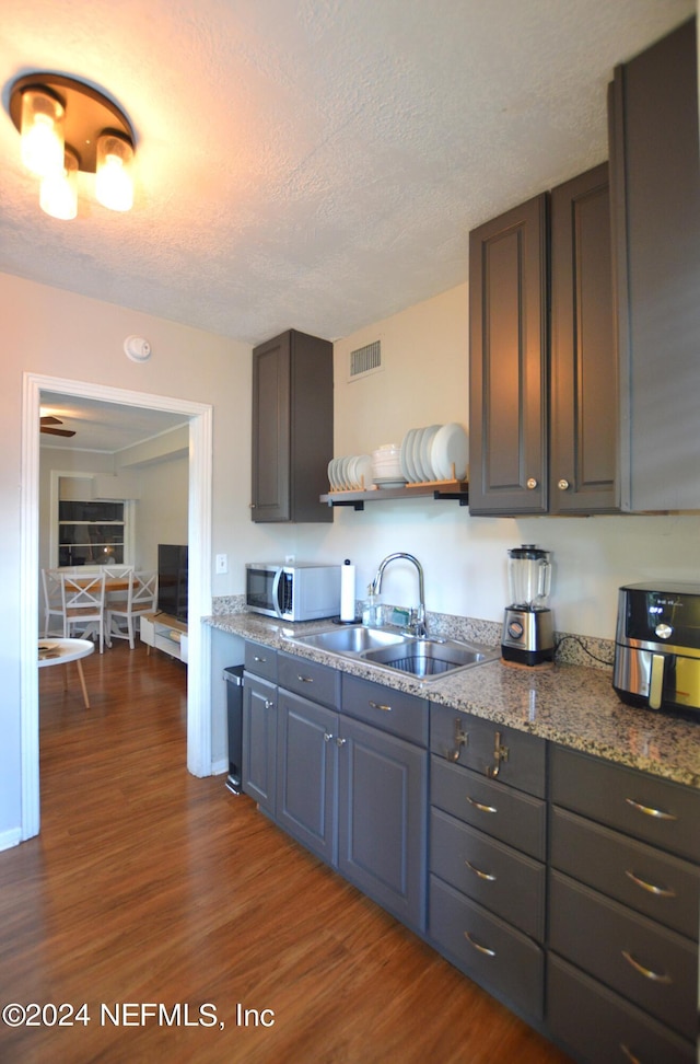 kitchen with sink, a textured ceiling, stone countertops, and hardwood / wood-style floors