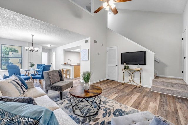 living room with a textured ceiling, sink, ceiling fan with notable chandelier, high vaulted ceiling, and light hardwood / wood-style flooring