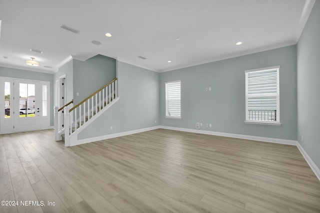 empty room featuring ornamental molding, light wood-type flooring, baseboards, and stairs