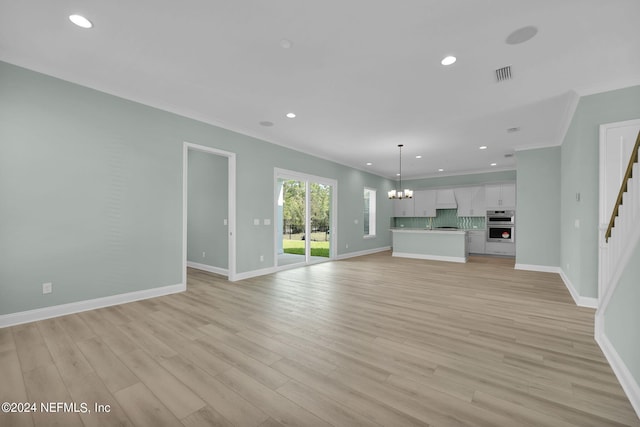 unfurnished living room with light wood finished floors, baseboards, visible vents, an inviting chandelier, and crown molding