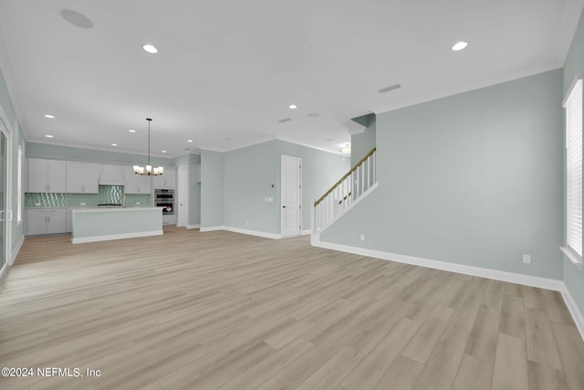 unfurnished living room with stairway, an inviting chandelier, ornamental molding, light wood-type flooring, and baseboards