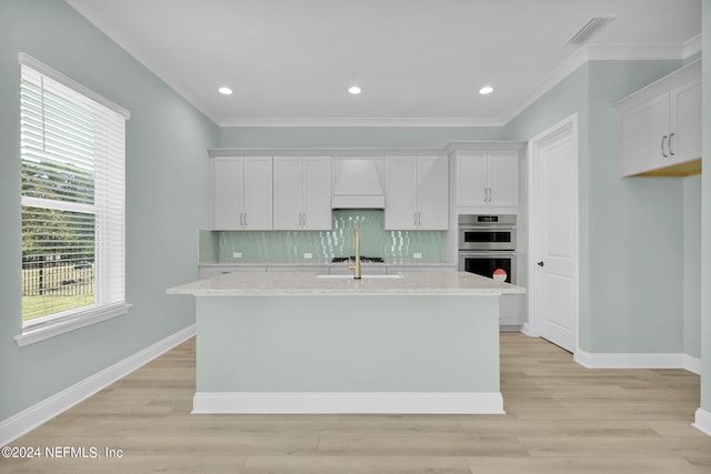 kitchen featuring custom exhaust hood, tasteful backsplash, visible vents, a kitchen island with sink, and white cabinets