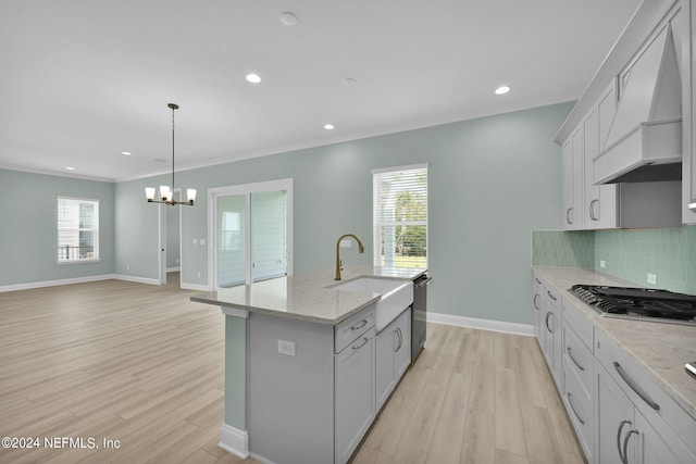 kitchen with a sink, light wood-style floors, appliances with stainless steel finishes, decorative backsplash, and custom range hood