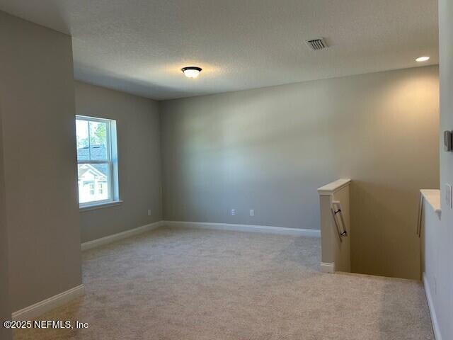 empty room featuring a textured ceiling, recessed lighting, light carpet, visible vents, and baseboards