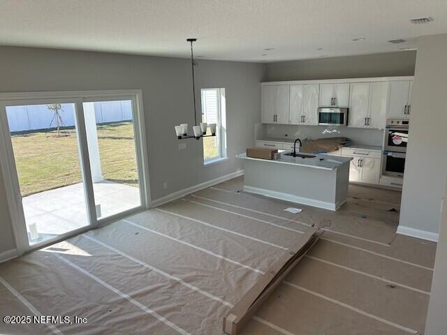 kitchen with baseboards, an island with sink, appliances with stainless steel finishes, white cabinetry, and a sink