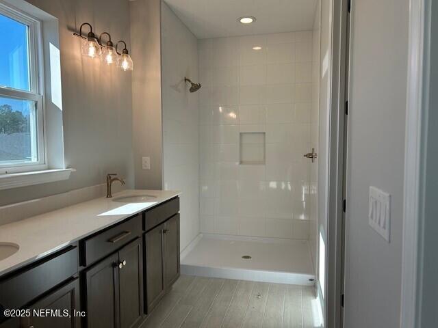 bathroom with double vanity, a tile shower, a sink, and wood finished floors