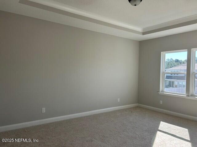 empty room with baseboards, a tray ceiling, and carpet flooring