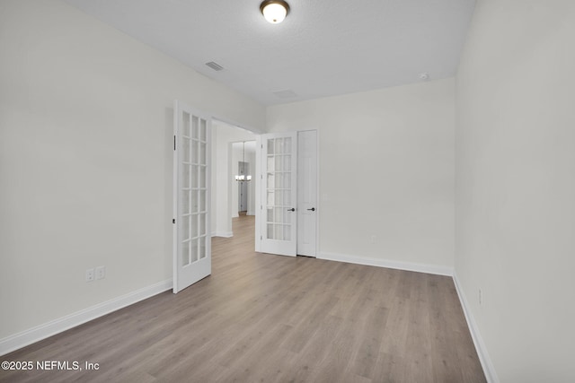 unfurnished room with light hardwood / wood-style flooring, a textured ceiling, and french doors