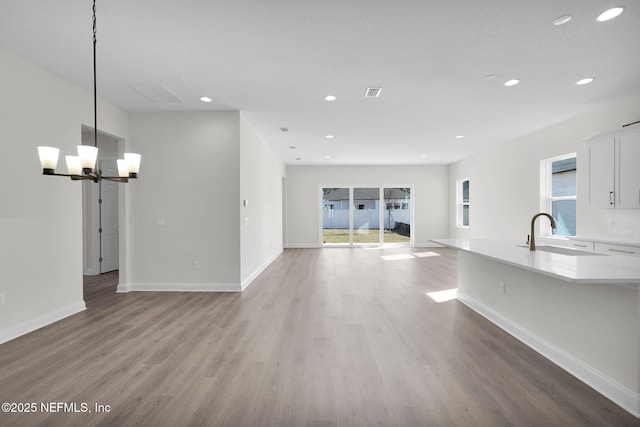 unfurnished living room with an inviting chandelier, wood-type flooring, and sink