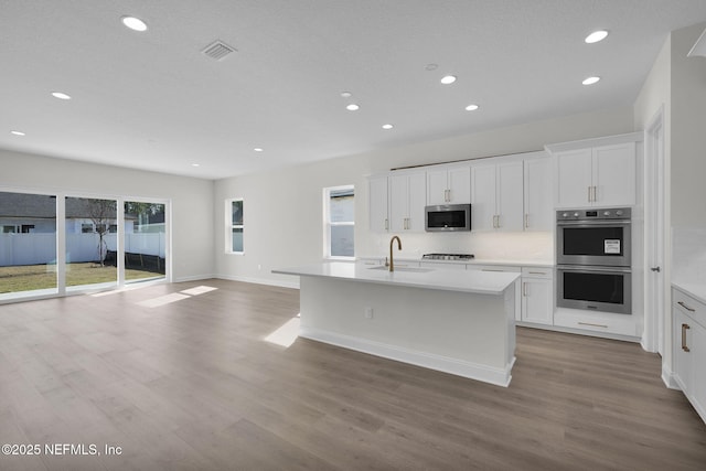 kitchen with stainless steel appliances, sink, white cabinetry, a center island with sink, and a healthy amount of sunlight