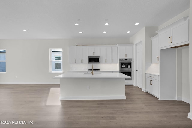 kitchen with white cabinetry, light hardwood / wood-style floors, stainless steel appliances, and an island with sink