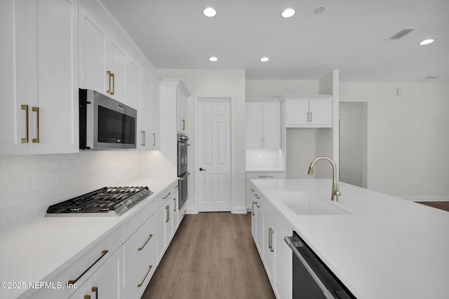 kitchen with sink, white cabinetry, light hardwood / wood-style flooring, appliances with stainless steel finishes, and decorative backsplash