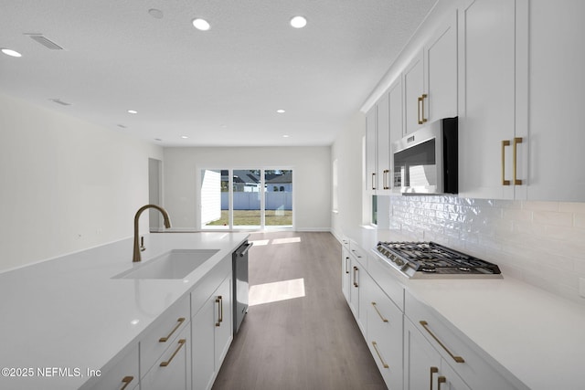 kitchen with sink, hardwood / wood-style flooring, white cabinetry, stainless steel appliances, and decorative backsplash