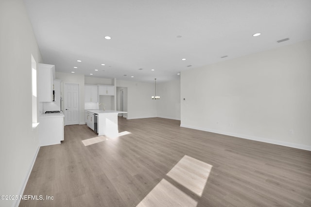 unfurnished living room featuring sink, a chandelier, and light hardwood / wood-style floors