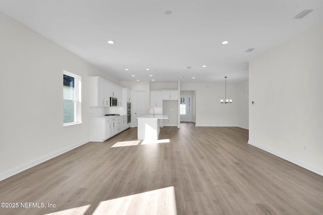 unfurnished living room featuring an inviting chandelier, sink, and light hardwood / wood-style flooring