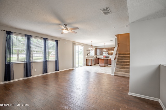 unfurnished living room featuring a textured ceiling, ceiling fan with notable chandelier, and dark wood-type flooring