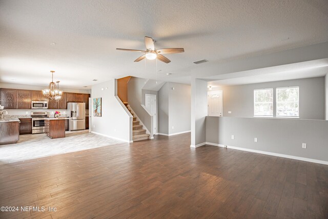 unfurnished living room featuring hardwood / wood-style floors, ceiling fan with notable chandelier, and a textured ceiling