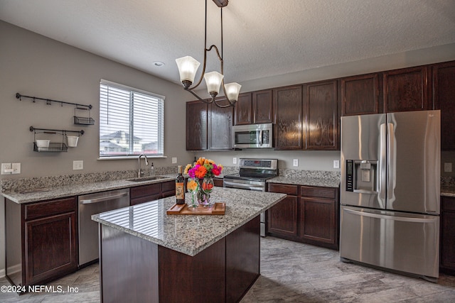 kitchen with a center island, sink, hanging light fixtures, light stone counters, and stainless steel appliances