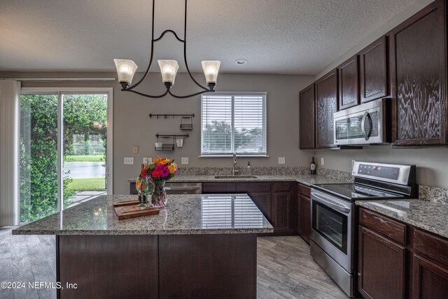 kitchen featuring light stone countertops, a center island, hanging light fixtures, a chandelier, and appliances with stainless steel finishes