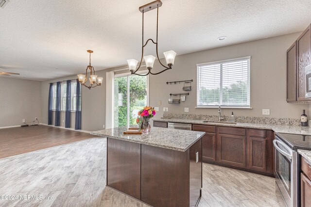 kitchen with light wood-type flooring, stainless steel appliances, sink, decorative light fixtures, and a center island