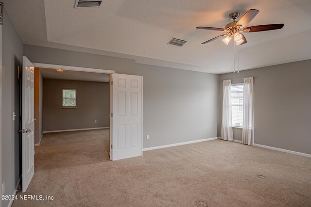 empty room featuring ceiling fan, light colored carpet, and a textured ceiling