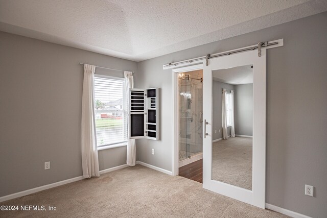 carpeted empty room with a textured ceiling, a barn door, and a wealth of natural light