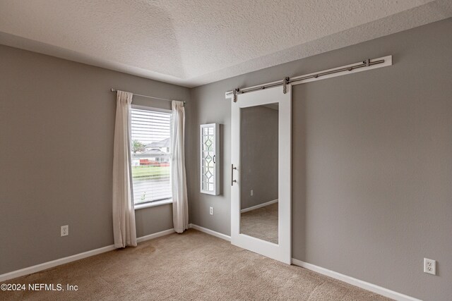 spare room with a textured ceiling, carpet floors, and a barn door