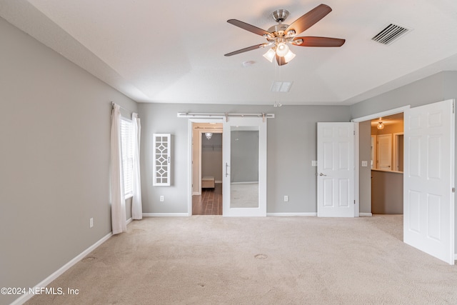 unfurnished bedroom featuring ceiling fan, a barn door, and light colored carpet