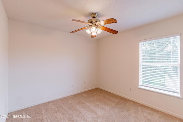 empty room with a wealth of natural light, ceiling fan, and light carpet