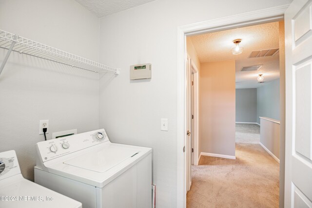 clothes washing area featuring washing machine and dryer, light carpet, and a textured ceiling