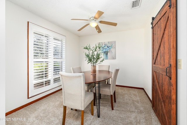 carpeted dining room with a barn door and ceiling fan