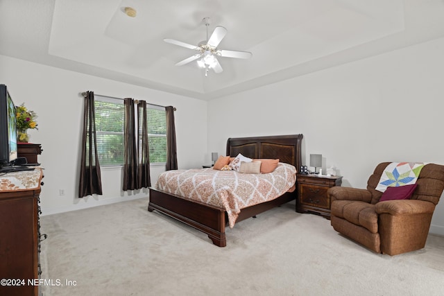 bedroom with ceiling fan, a tray ceiling, baseboards, and light colored carpet