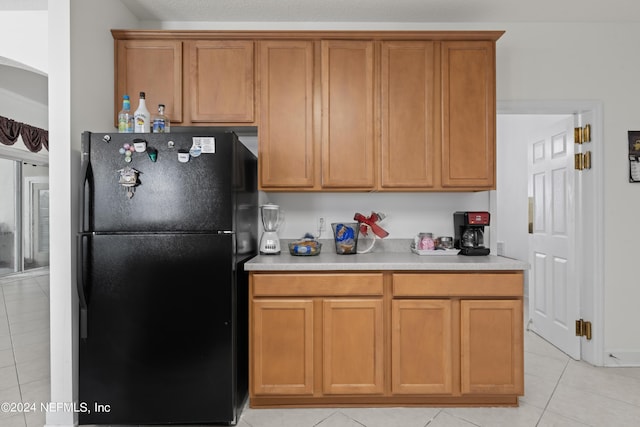 kitchen with light countertops, brown cabinetry, light tile patterned flooring, and freestanding refrigerator