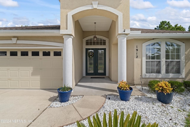 view of exterior entry with french doors, roof with shingles, stucco siding, concrete driveway, and an attached garage