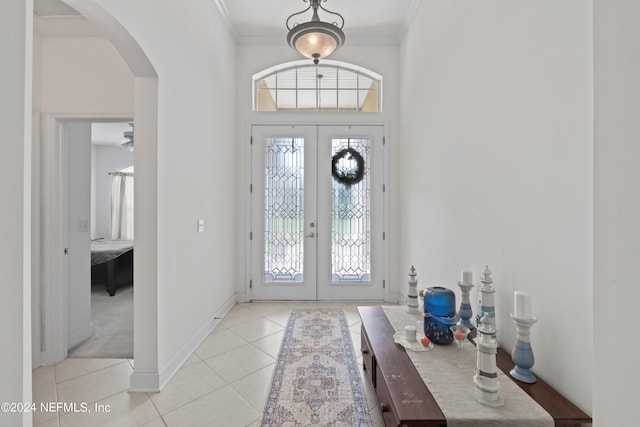 entryway featuring arched walkways, french doors, light tile patterned floors, ornamental molding, and baseboards