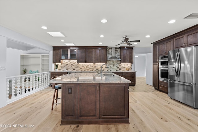 kitchen featuring light wood-type flooring, stainless steel appliances, ceiling fan, and wall chimney range hood