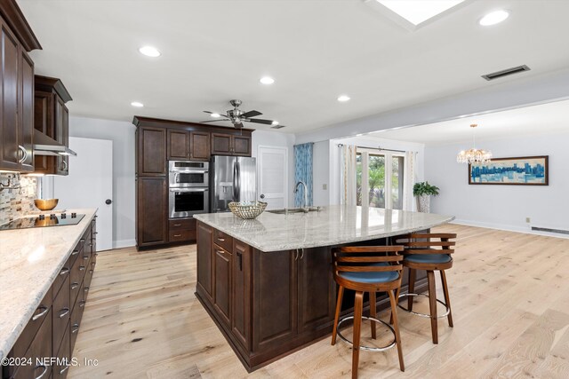 kitchen featuring stainless steel appliances, light stone counters, ceiling fan with notable chandelier, and light wood-type flooring