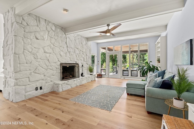 living room featuring light wood-type flooring, beamed ceiling, ceiling fan, and a stone fireplace