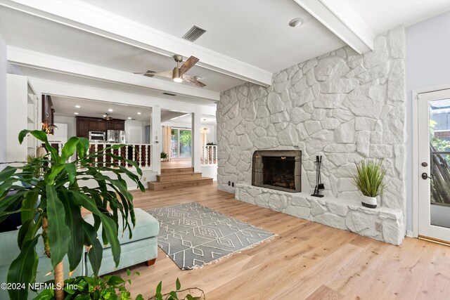 living room with light hardwood / wood-style floors, ceiling fan, a fireplace, and beam ceiling