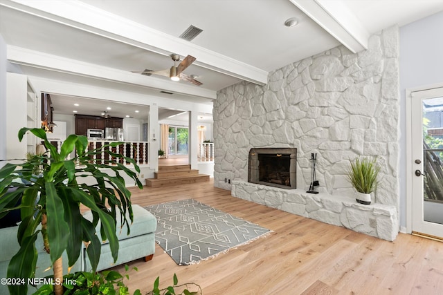 living area featuring beam ceiling, a fireplace, visible vents, a ceiling fan, and wood finished floors