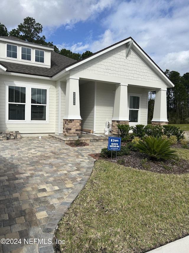 95246 Golden Glow Dr, Fernandina Beach, FL 32034 - craftsman-style home with stone siding, roof with shingles, covered porch, and a front lawn